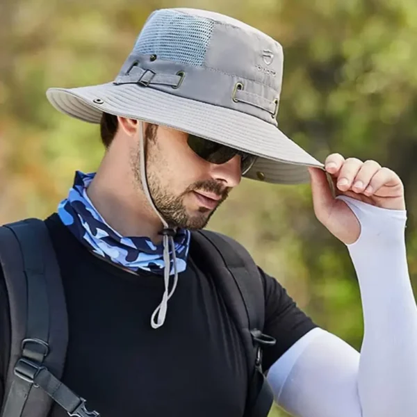 Un homme de profil tient la visière de son bob chapeau dans un décor de nature flouté
