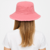 Un modèle porte un bob ficelle rose de dos pour montrer l'arrière du chapeau avec un décor blanc