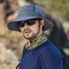 Un homme porte des lunettes de soleil et un bob chapeau dans un décor de nature flouté