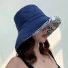 Une femme porte un bob chapeau élégant bleu marine sur un décor clair et lumineux