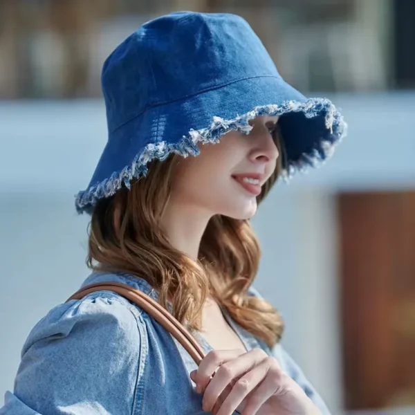 Une femme souriante de profil porte un magnifique bob chapeau en jean bleu sur un décor flouté extérieur