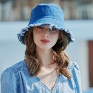 Une femme souriante de face porte un magnifique bob chapeau en jean bleu sur un décor flouté extérieur