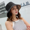 Une femme porte un bob chapeau réversible noir avec une doublure style léopard sur un décor grisé