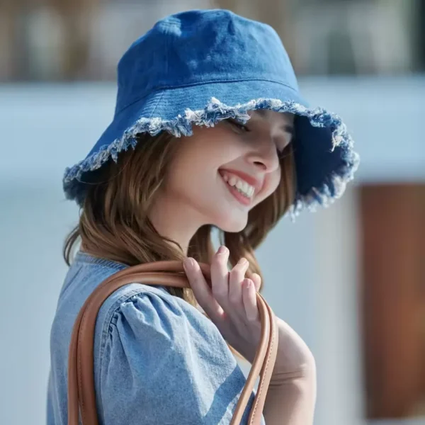 Une femme souriante porte un magnifique bob chapeau en jean bleu sur un décor flouté extérieur