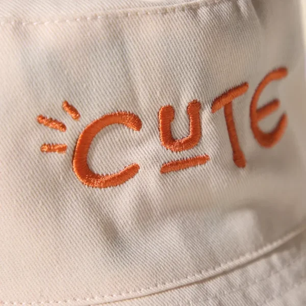 Zoom sur une inscription brodée en orange "so cute" d'un bob chapeau