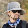 Un modèle avec des lunettes noires de soleil porte un joli chapeau bob pêche sur la tête sur un décor de nature flouté