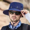 Un modèle avec des lunettes noires de soleil porte un joli chapeau bob pêche couleur bleu marine sur la tête sur un décor de nature flouté