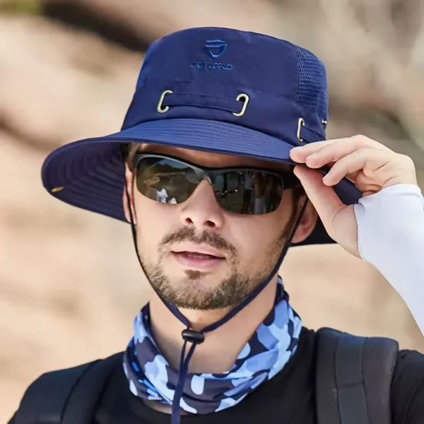 Un modèle avec des lunettes noires de soleil porte un joli chapeau bob pêche couleur bleu marine sur la tête sur un décor de nature flouté