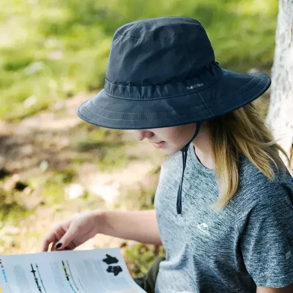 Une femme lit un magazine à l'ombre d'un arbre et porte un chapeau bob bleu