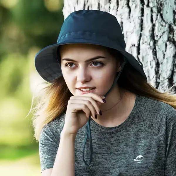 Une femme porte un bob chapeau et prend la pose devant un arbre