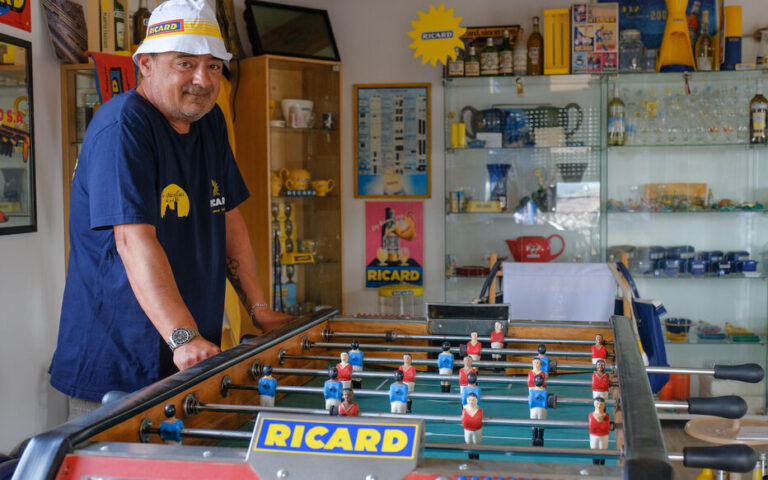 Un marseillais qui porte le véritable bob ricard fait une partie de baby foot dans un bistro de marseille