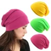 Un modèle féminin de profil porte un bonnet coton rose sur fond balnc avec 3 autres variantes, jaune, vert et rose présentées à côté