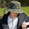 Un homme prend la pose la tête baissée avec un bob chapeau vert anti uv sur sa tête avec un décor de verdure flouté en arrière-plan