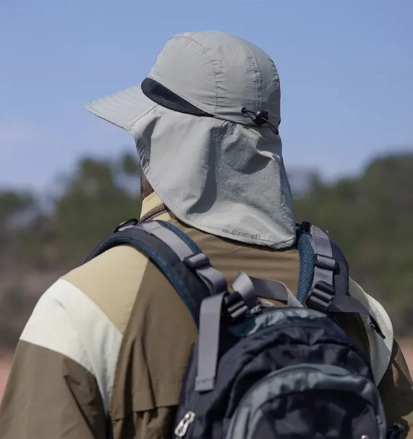 Un homme style aventurier de dos porte un bob randonnée avec une extension de protection pour la nuque sur un décor de nature