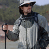 Un homme style aventurier bien équipé pour la randonnée porte un bob chapeau et des lunettes de soleil sur un décor de nature