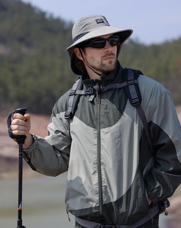 Un homme style aventurier bien équipé pour la randonnée porte un bob chapeau et des lunettes de soleil sur un décor de nature