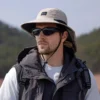 Un homme style aventurier porte un bob randonnée et des lunettes de soleil sur un décor de nature