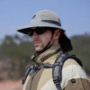 Un homme style aventurier porte un bob randonnée et des lunettes de soleil sur un décor de nature
