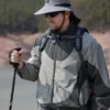 Un homme style aventurier bien équipé pour la randonnée porte un bob chapeau et des lunettes de soleil sur un décor de nature