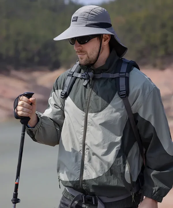 Un homme style aventurier bien équipé pour la randonnée porte un bob chapeau et des lunettes de soleil sur un décor de nature