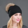 Modèle de profil porte un bonnet noir à pompons pour femme sur fond gris foncé