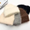 Plusieurs bonnets alpaga en laine naturelle de différentes couleurs, dont crème, gris, marron et noir, disposés ensemble sur une table blanche.