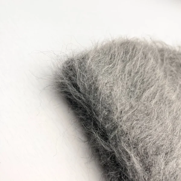 Gros plan sur un bonnet en alpaga gris avec une texture duveteuse et poils longs, photographié sur fond blanc pour montrer la matière douce et chaude.