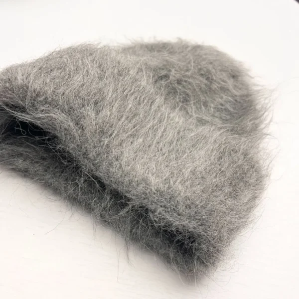 Bonnet chaud en laine grise, au toucher moelleux et chaud, posé sur une table blanche, idéal pour l’hiver et les temps froids.