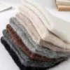 Pile de bonnets en alpaga pliés, montrant différentes teintes naturelles comme beige, gris, marron et noir, soulignant la douceur de la laine d’alpaga.