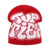 Bonnet de ski pour homme rouge avec un texte graffiti blanc au style urbain, parfait pour affirmer sa personnalité en montagne.