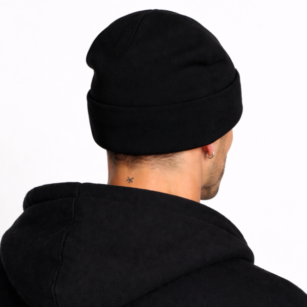 Un modèle porte un bonnet en laine noir de dos fond clair