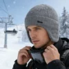Modèle homme en station de ski portant un bonnet gris cache oreilles, accessoire chaud pour sports d’hiver